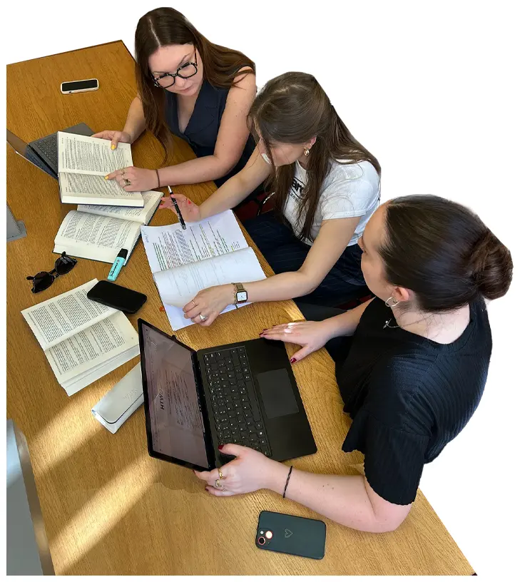 Studenten sitzen an einem Tisch mit Laptop und Lernmaterialien